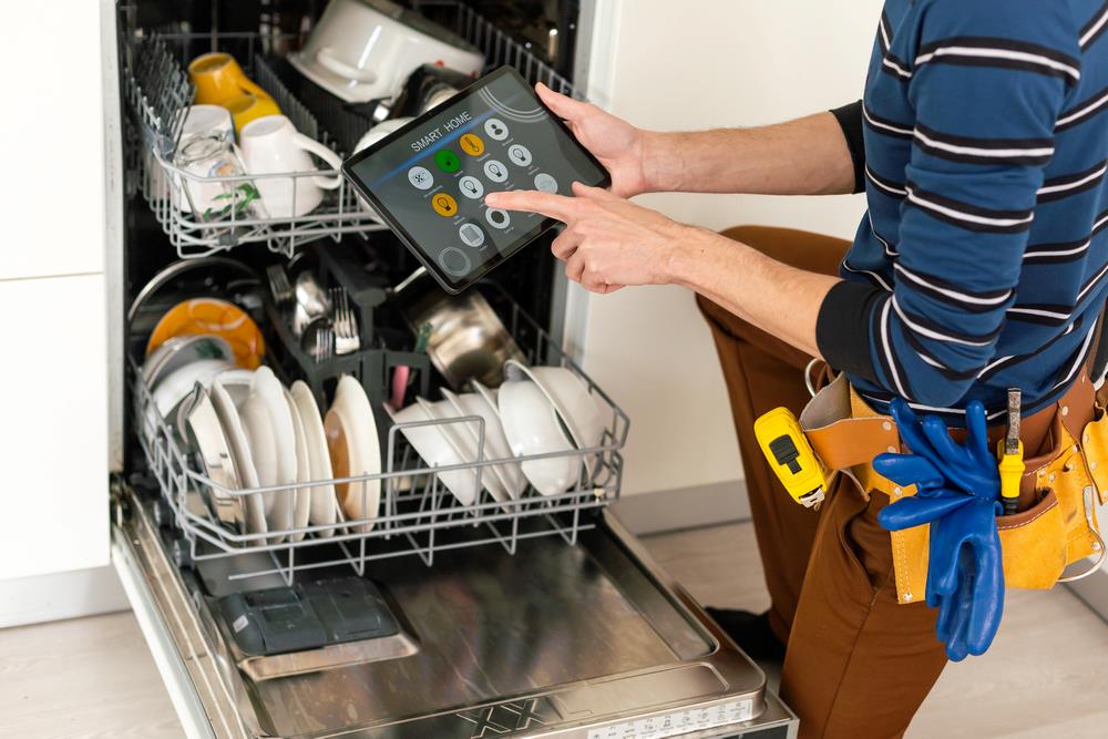 Dishwasher repairs Handyman using a tablet PC while repairing a household dishwasher, featuring Accurate Appliance Repair and highlighting dishwasher repairs, in line with the page’s focus on expert appliance service solutions.<br />