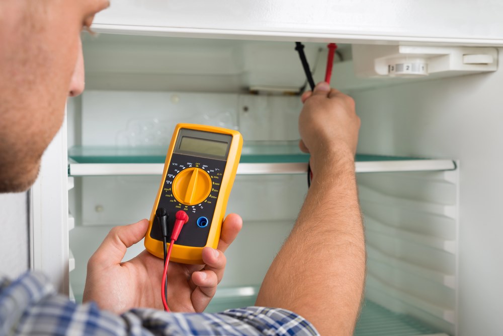 How Our Refrigerator Repair Service Works Image of a technician checking a refrigerator with a multimeter, featuring Accurate Appliance Repair and highlighting how their refrigerator repair service works to diagnose and fix issues efficiently.