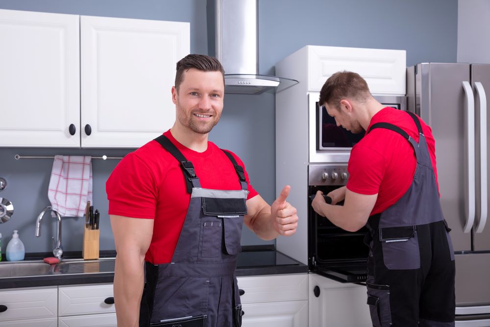 Our story Technician showing a thumbs-up sign in front of his assistant, featuring Accurate Appliance Repair and highlighting "Our Story," reflecting the team's professionalism and commitment to quality service.<br />